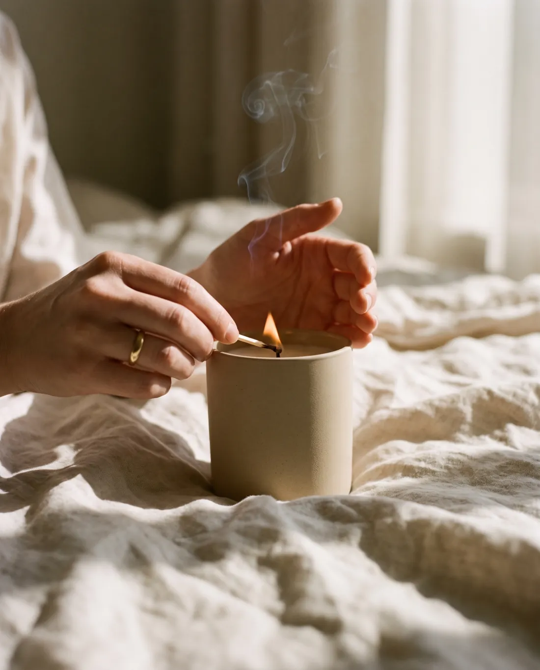 Manos encendiendo una vela aromática sobre ropa de cama de lino